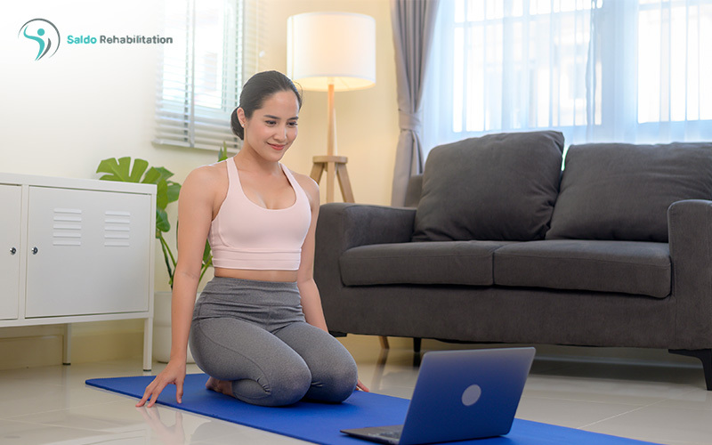 Woman doing yoga at home with laptop open